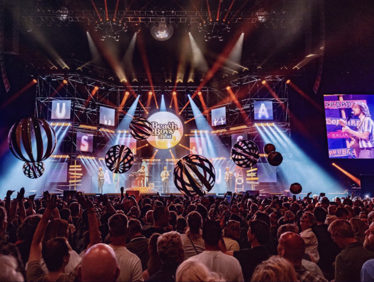 Concertpodium met grote gestreepte ballen boven het publiek en een tributeband op het podium
